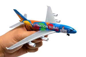 Colorful model airplane with 'Destination Dubai' text held in a hand against a white background