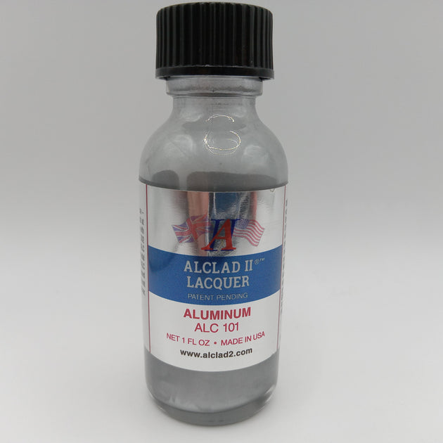A small clear bottle of Alclad II Lacquer Aluminum Lacquer (ALC 101) with a black ribbed cap and a white, blue, and red label, set against a neutral gray background.